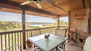 A covered outdoor area with a table and chairs, a ceiling fan, and a view of a lake and trees.