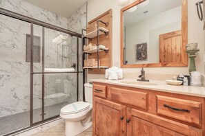 Un baño con cabina de ducha de vidrio, paredes de mármol, tocador de madera y un espejo grande.