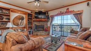 A cozy living room with a fireplace, wooden shelves, a large plush sofa, and a balcony with a view. - 2BR Village At Indian Point 1607 near SDC - Free Tickets Daily up to $500 (Branson)