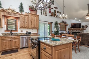 Una cucina con mobili in legno, un piano di lavoro in granito, un piano cottura integrato e una zona pranzo con camino.