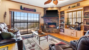 A cozy living room with a fireplace, leather furniture, and a large window overlooking a scenic view.