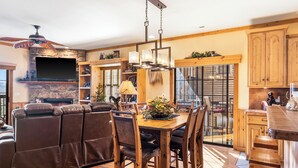 A spacious living room with a fireplace, leather sofa, dining table with chairs, and a kitchen area with wooden cabinets and a bar.