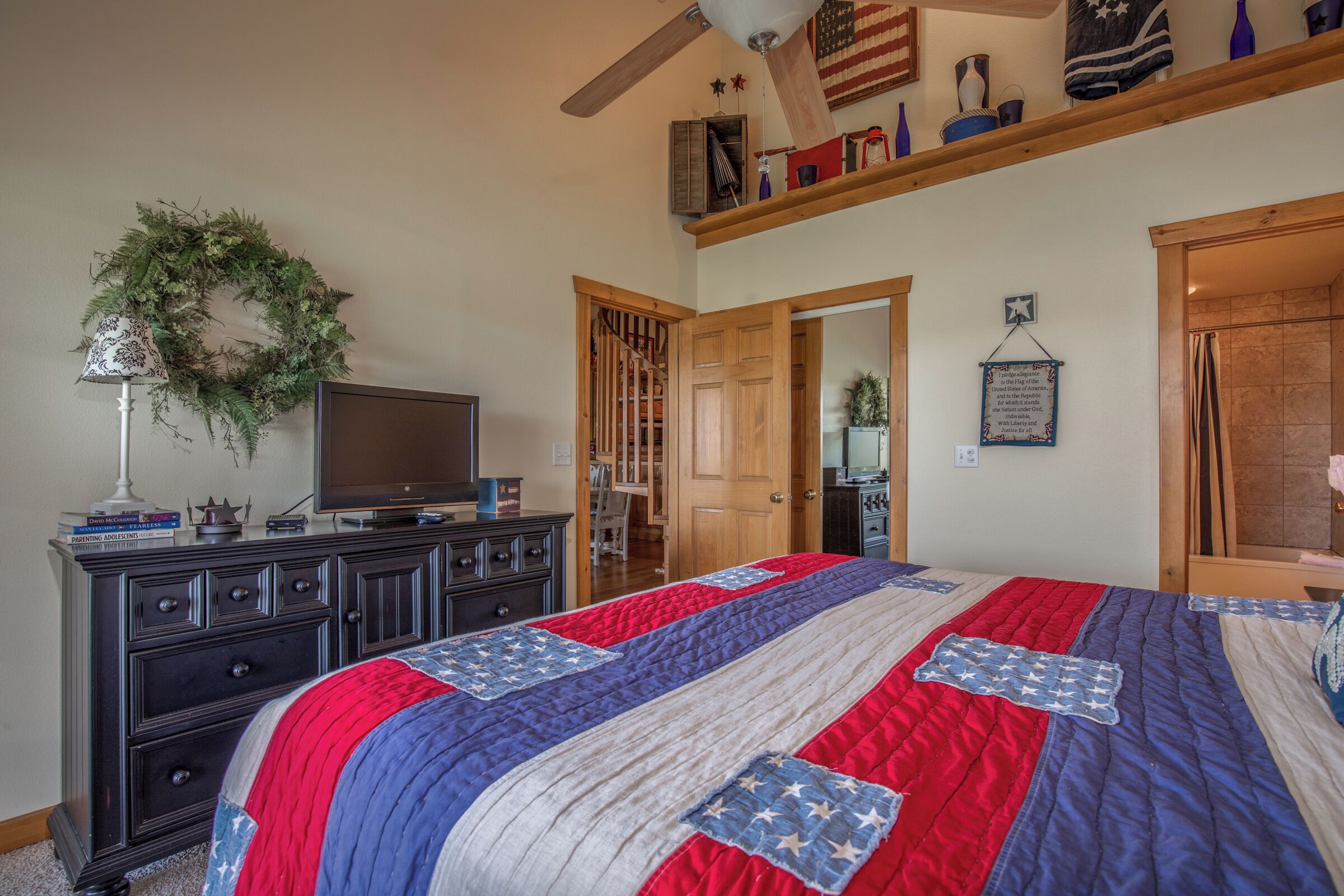 Une chambre à coucher avec un lit recouvert d’une courtepointe ornée d’un motif en étoile, une commode, un téléviseur et une guirlande décorative accrochée au mur.