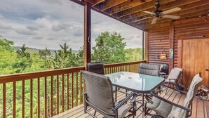 A wooden deck with a glass table and chairs, a ceiling fan, and a view of the surrounding forest. - 2BR Village At Indian Point 1702 next to SDC- Free Tickets Daily up to $500 (Branson)