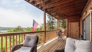 A wooden deck with wicker chairs and a table, overlooking a scenic landscape with an American flag. - 2BR Village At Indian Point 1704 near SDC - Free Tickets Daily up to $500 (Branson)