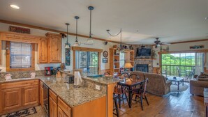 A spacious kitchen with granite countertops, wooden cabinets, and a central island. There is a dining area with a table and chairs, and a large window offering a view of the outdoors. - 2BR Village At Indian Point 1705 near SDC - Free Tickets Daily up to $500 (Branson)