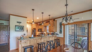 A kitchen with wooden cabinets, a central island with stools, pendant lighting, and a view through large windows. - 2BR Village At Indian Point 1705 near SDC - Free Tickets Daily up to $500 (Branson)