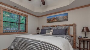 A bedroom with a large bed, a wooden headboard, a window with blinds, a painting on the wall, and a nightstand with a lamp. - 2BR Village At Indian Point 1706 near SDC - Free Tickets Daily up to $500 (Branson)