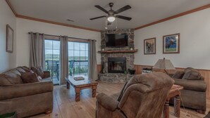 A living room with a stone fireplace, a ceiling fan, and a large TV mounted on the wall. - 2BR Village At Indian Point 1706 near SDC - Free Tickets Daily up to $500 (Branson)