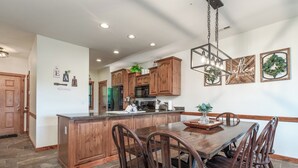A spacious kitchen with wooden cabinets, a central island, and a dining area with wooden chairs. - 2BR Village At Indian Point 1707 near SDC - Free Tickets Daily up to $500 (Branson)