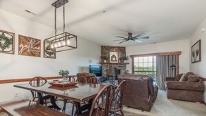 A spacious living room with a fireplace, a dining area with wooden furniture, and a balcony with a view. - 2BR Village At Indian Point 1707 near SDC - Free Tickets Daily up to $500 (Branson)