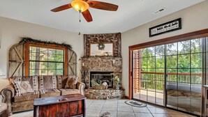 A cozy living room with a stone fireplace, large windows, and a ceiling fan. - 2BR Village At Indian Point 1801 near SDC - Free Tickets Daily up to $500 (Branson)