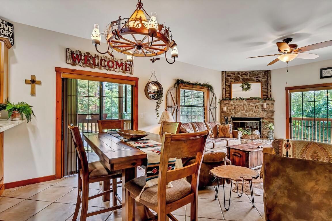 A spacious living room with a fireplace, a dining area with a wooden table and chairs, and a large chandelier.