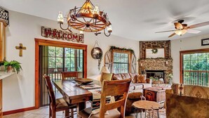 A spacious living room with a fireplace, a dining area with a wooden table and chairs, and a large chandelier. - 2BR Village At Indian Point 1801 near SDC - Free Tickets Daily up to $500 (Branson)