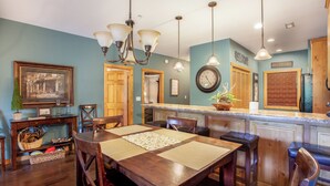A dining area with a wooden table, chairs, and a decorative centerpiece. There is a kitchen area with a clock and a welcome sign. - 2BR Village At Indian Point 1803 near SDC - Free Tickets Daily up to $500 (Branson)