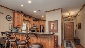 A kitchen with wooden cabinets, a central island with stools, a clock, and a refrigerator. - 2BR Village At Indian Point 1904 near SDC - Free Tickets Daily up to $500 (Branson)