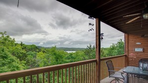 Eine Holzterrasse mit Tisch und Stühlen, mit Blick auf einen bewaldeten Bereich und einen See.