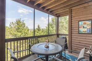 Eine Holzterrasse mit rundem Tisch und Stühlen, einem Holzgeländer und Blick auf Bäume.