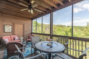 Une terrasse en bois, meublée de meubles en osier, avec une table ronde et un ventilateur de plafond.