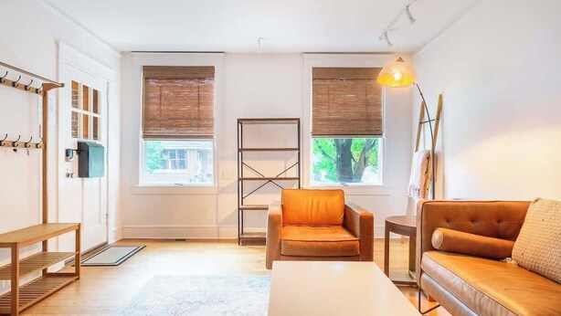 A modern living room with a sofa, armchair, and coffee table. There are two windows with blinds, a coat rack, and a lamp. - Bright, clean spacious 2 BR apt off street parking (Wilmington)