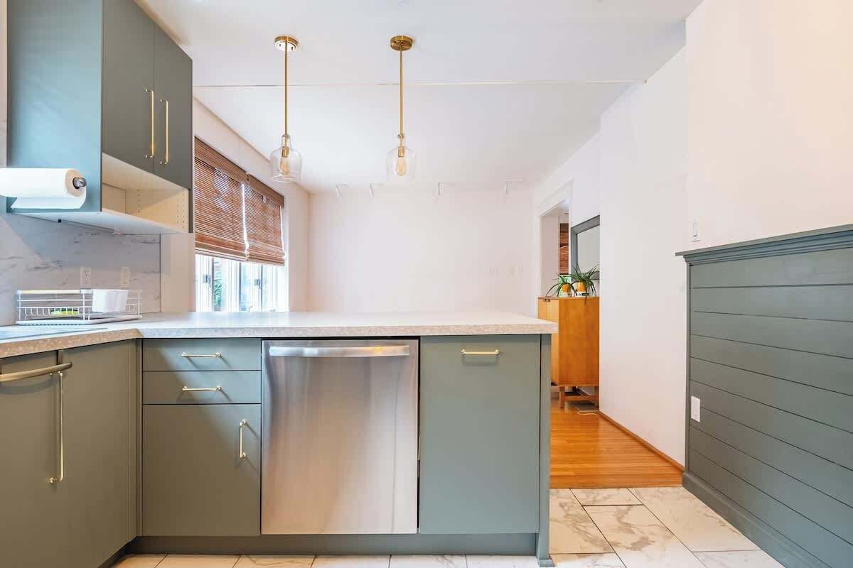 Une cuisine moderne avec des meubles gris, un lave-vaisselle en acier inoxydable et des luminaires suspendus.