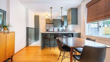 Une cuisine moderne avec un coin repas, un plancher en bois et une fenêtre équipée de stores.