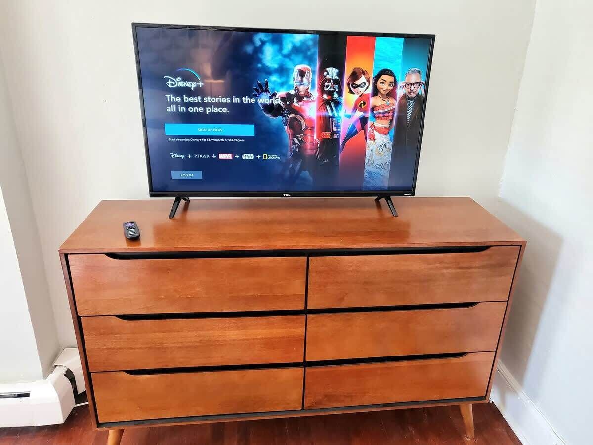 Ein Flachbildfernseher steht auf einer Holzkommode, auf der ein Fernbedienung liegt.