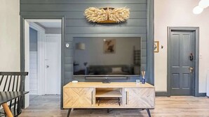 Una sala de estar con un televisor de pantalla plana grande montado en una pared oscura, un mueble bajo de madera y un sillón negro a la izquierda.