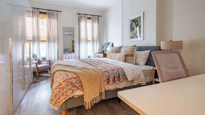 Un dormitorio con cama, mesita de noche, silla y un cuadro en la pared.