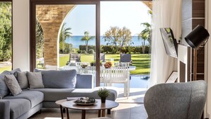 Ein modernes Wohnzimmer mit einem großen Glasfenster zum Poolbereich, einem grauen Sofa, einem Couchtisch und einem an der Wand befestigten Flachbildfernseher.