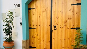 En pardörr av trä med ett handtag av metall, flankerad av två terrakotta-krukor med växter, och en skylt med siffran ”10B” ovanför.
