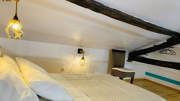 A bedroom with a large bed, two wall-mounted lights, a wooden chair, and a small table. - Adega dos Moinhos (Cadaval)