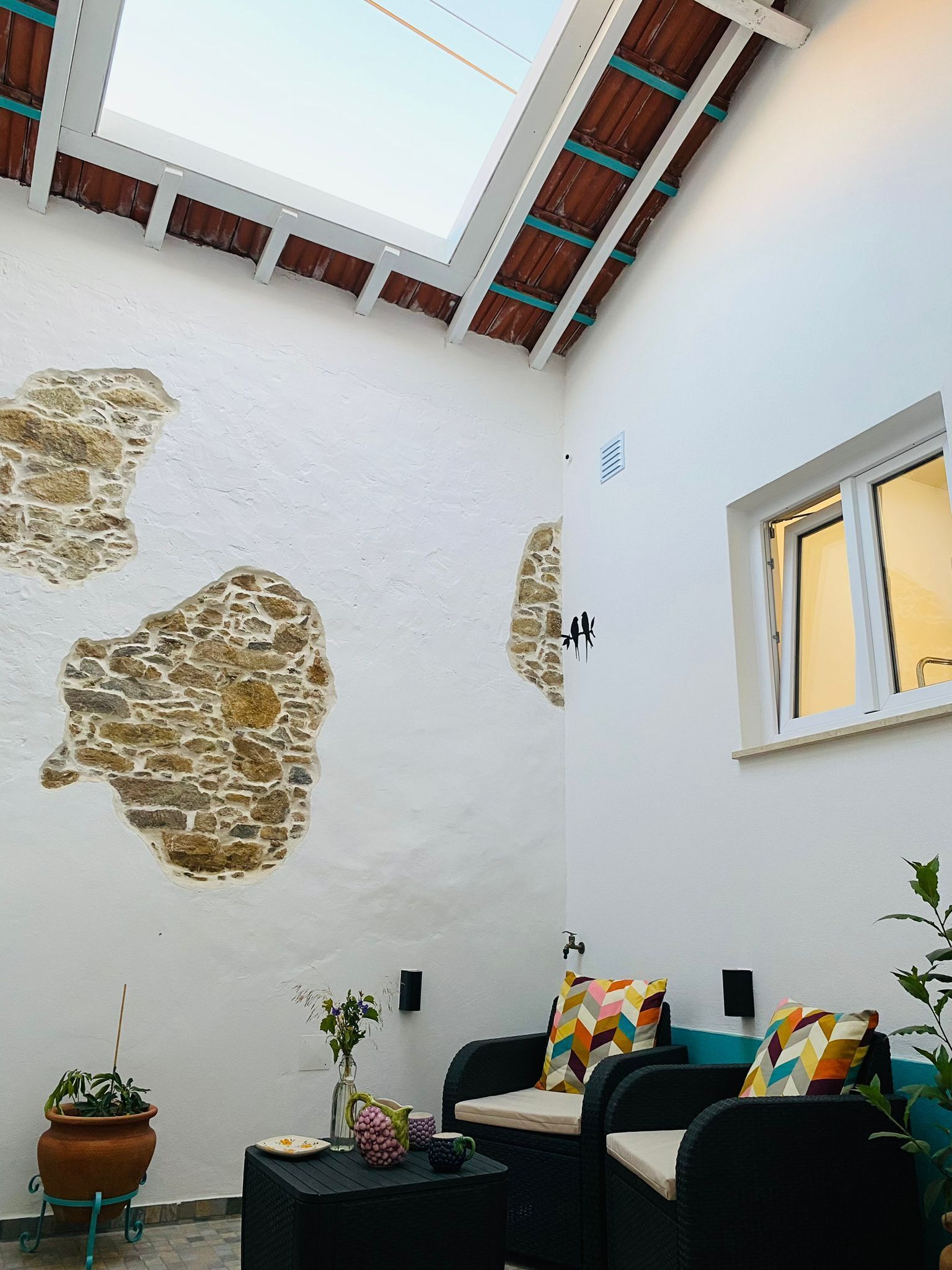 A room with a sloped ceiling, stone wall patches, a window, and a seating area with cushions.