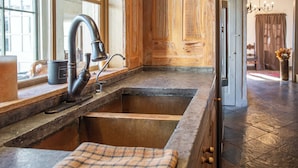 A rustic kitchen with a wooden countertop, a large sink, and a plaid towel. - Charming Hill Country Getaway in Texas (Fredericksburg)