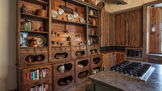 A rustic kitchen with wooden cabinetry, a gas stove, and shelves filled with kitchenware and books. - Charming Hill Country Getaway in Texas (Fredericksburg)