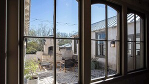 A room with large windows overlooking a courtyard with outdoor furniture and a stone structure. - Charming Hill Country Getaway in Texas (Fredericksburg)