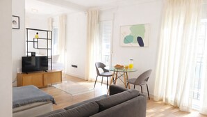 A modern living room with a sofa, a TV, a glass table, and a dining area. - Collection Madrid Rio Exterior 3 Personas (Madrid)