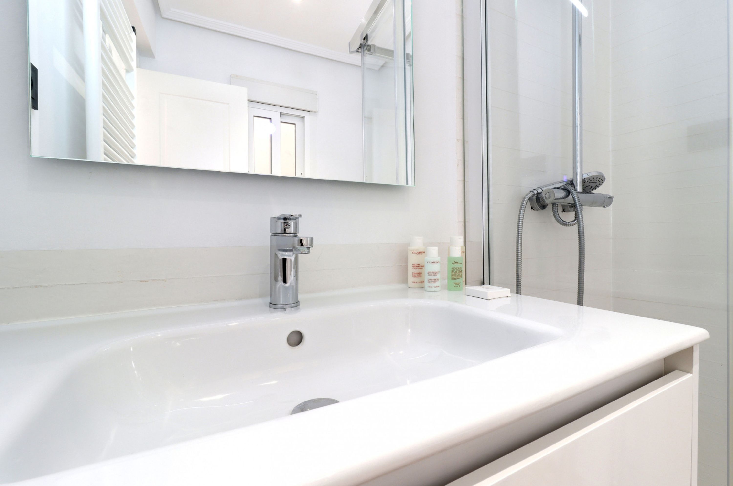 A modern bathroom with a large white sink, a mirror, and a glass-enclosed shower area.