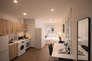 Una habitación de hotel compacta con kitchenette, una cama, zona de comedor y baño.