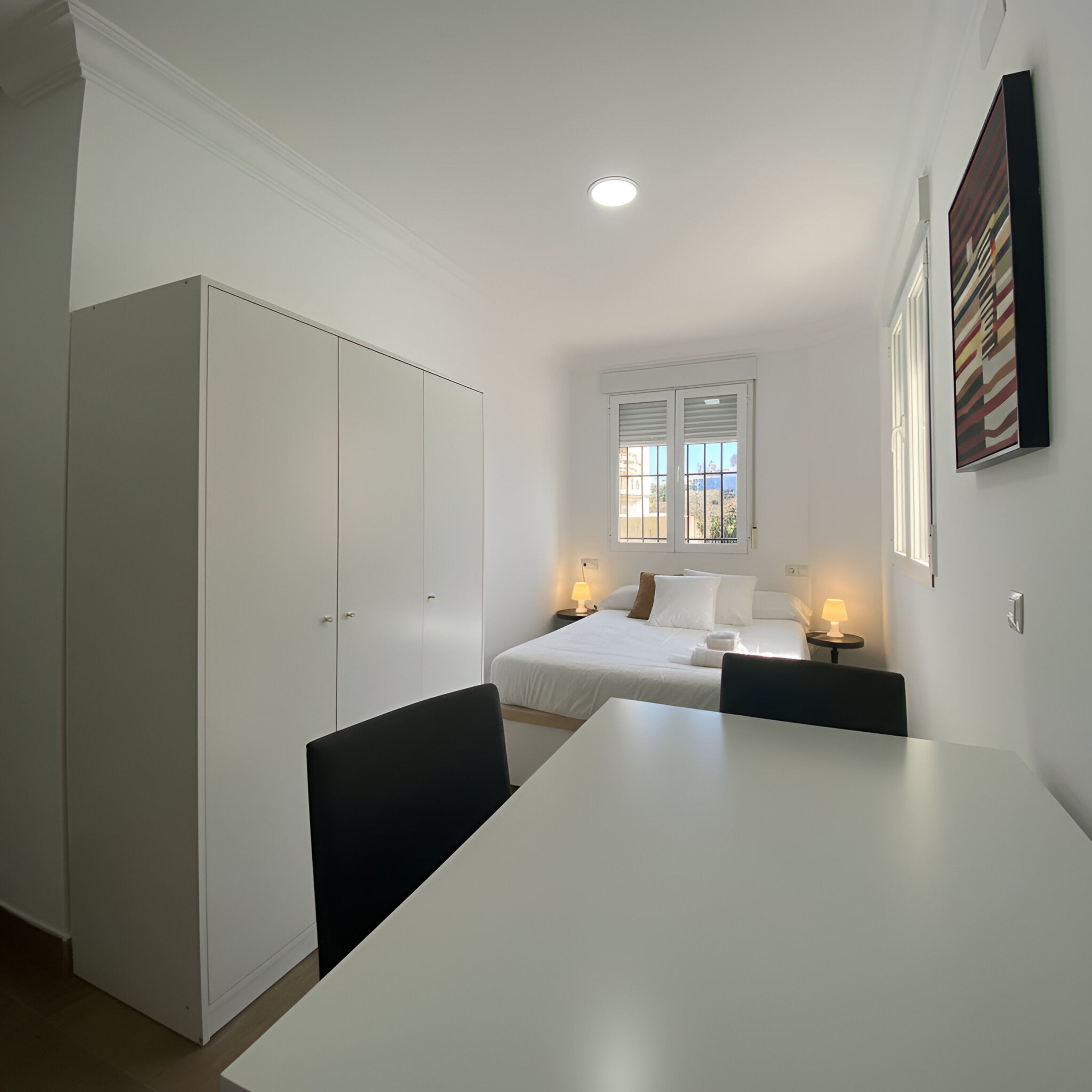 Un dormitorio con cama, mesitas de noche, armario y ventana con persianas.