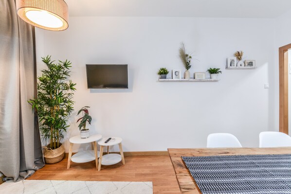 A modern living room with a wooden table, white chairs, a TV mounted on the wall, and a potted plant. - C Plaza de Espa a 3A (Madrid)
