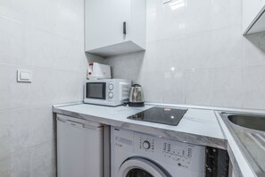 A compact kitchen with a washing machine, microwave, and a coffee maker. - C Plaza de Espa a 3A (Madrid)