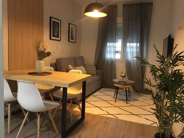 A modern living room with a wooden dining table, white chairs, a grey sofa, and a small side table with a vase. - C Plaza de Espa a 3A (Madrid)