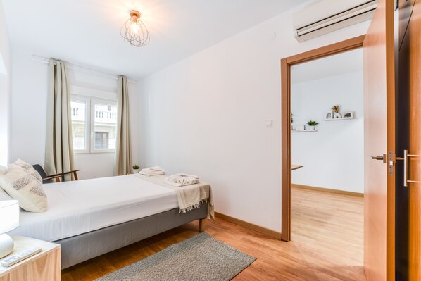 Un dormitorio con cama, mesita de noche, lámpara y vistas al exterior a través de una ventana.