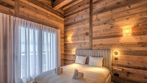 A neatly made bed with pillows and towels, wooden walls, and a window with curtains.