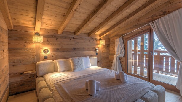 A wooden cabin room with a bed, two wall-mounted lights, and a large window with curtains.