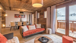 A cozy cabin interior with a wooden ceiling, a dining area, and a balcony with a view.