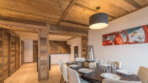 A dining area with a wooden ceiling, a painting of a skier, and a staircase leading to another room.