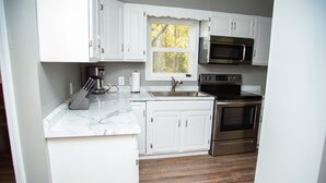 Una cocina compacta con armarios blancos, horno de acero inoxidable, microondas y cafetera.