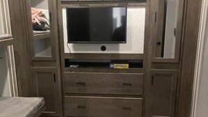 Una stanza con televisore integrato su un mobile in legno, una panca e un pavimento tappezzato.